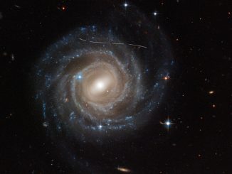 Den här bilden från Hubbles rymdteleskop av den spärrade spiralgalaxen UGC 12158 ser ut som om någon har använt en vit märkpenna. I själva verket är det en kombination av tidsexponeringar av en asteroid i förgrunden som rör sig genom Hubbles synfält och fotobombar observationen av galaxen. Flera exponeringar av galaxen togs, vilket framgår av det streckade mönstret. Asteroiden visas som ett böjt spår på grund av parallax eftersom Hubble inte är stillastående utan kretsar kring jorden, vilket ger en illusion av att den svaga asteroiden simmar längs en böjd bana. Den okarterade asteroiden befinner sig i asteroidbältet i vårt solsystem och är därför 10 biljoner gånger närmare Hubble än bakgrundsgalaxen. I stället för att vara en olägenhet är den här typen av data användbar för astronomer som vill göra en inventering av asteroidpopulationen i vårt solsystem. Kredit: NASA, ESA, Pablo García Martín (UAM); Bildbehandling: Joseph DePasquale (STScI); Erkännande: Alex Filippenko (UC Berkeley)